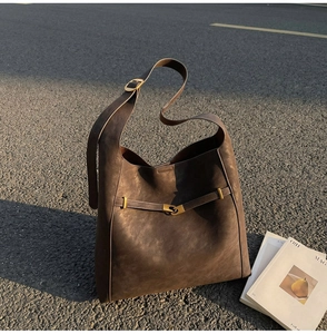 Close-up of matte dark brown leather texture and golden buckle on large hobo bag