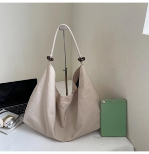 Detail of light beige hobo bag with drawstring strap and wooden bead accents on metal stand
