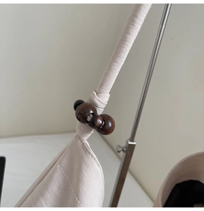 Detail of knot design and dark brown wooden beads on beige canvas shoulder bag strap