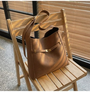 Detail shot of a brown leather bucket bag featuring a polished metal buckle and wide strap