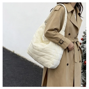 Detail of white quilted puffer tote bag worn over a khaki trench coat in winter setting