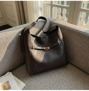 Detail view of a large brown bucket bag with gold buckle on a sofa corner