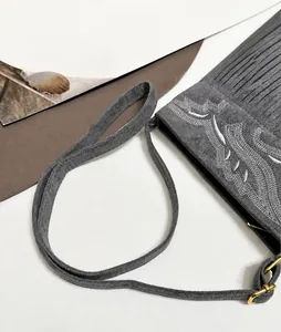 Vista detallada del bolso de ante gris con bordado blanco y flecos largos de estilo bohemio