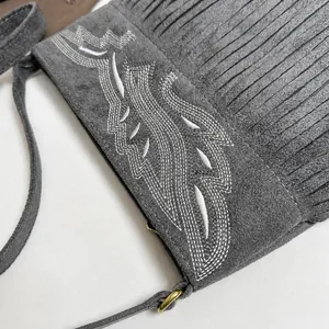 Detalle de bolso en ante gris con bordados blancos y acabado de flecos decorativos