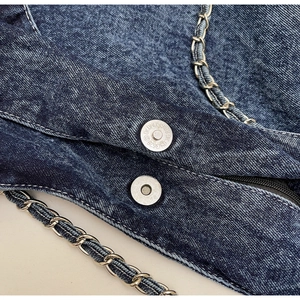 Detail of vintage blue denim bag featuring silver metal chain and magnetic snap closure