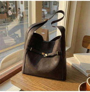 Detailed macro view of dark brown suede bucket bag with gold buckle on wooden table