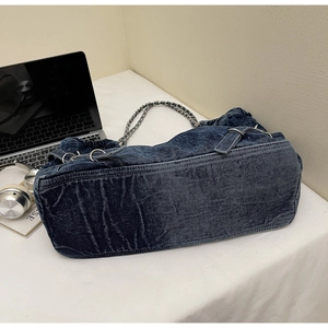 Detail of blue washed denim shoulder bag with silver chain strap on a white desk