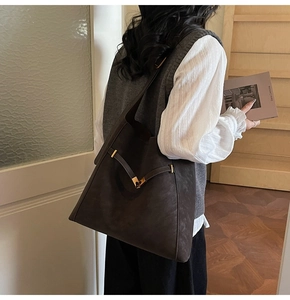 Close-up of brown leather bucket bag featuring a decorative V-shaped metal buckle detail
