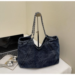 Detail of blue washed denim bag featuring silver metal chain strap and drawstring closure