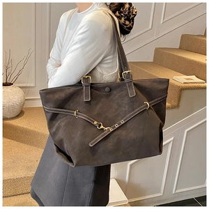 Detail van vintage shopper met contraststiksels en gouden gesp op donkere suède stof