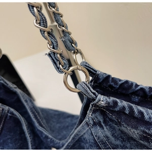 Detail of silver metal chain interwoven with dark blue denim fabric on the shoulder strap