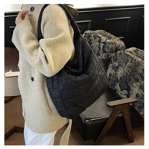Side view of a large black quilted puffer shoulder bag worn by a model in a stylish room