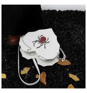 Detail der weißen Spinnennetz-Tasche mit roter Strass-Spinne auf dunklem Steingrund
