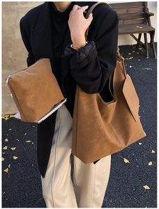 Brown suede tote bag with white stitching shown on a shoulder in an autumn setting