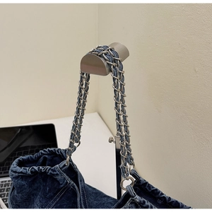 Detail of blue denim fabric texture and woven silver metal chain strap on shoulder bag