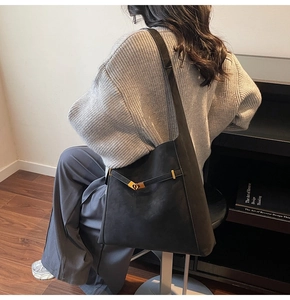Detail of a large black matte tote bag with a gold metal buckle on a shoulder strap