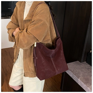 Detail der burgunderroten Hobo-Tasche aus Wildleder mit weißen Kontrastnähten und Goldteilen
