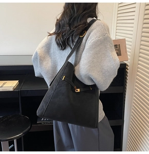 Detail view of large black bucket bag with gold clasp shown on a grey sweater