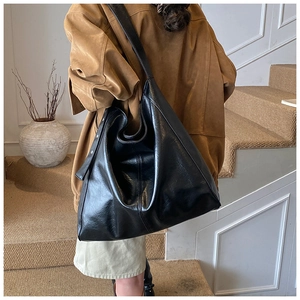 Chic large black hobo tote bag in glossy leather worn by model on stairs