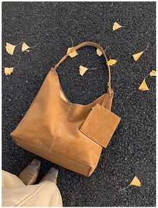 Detail of brown suede Hobo bag with white stitching and matching mini pouch on autumn leaves