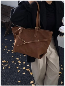 Detail van donkerbruine leren tote bag met gouden gesp in een herfstachtige setting