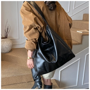 Detailed side view of black glossy oversized tote bag with soft leather texture and wide strap