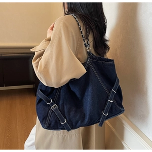 Detail of large dark blue denim tote bag with silver chain strap and metal buckles