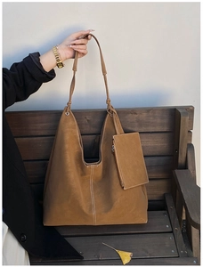 Close-up of brown hobo tote bag with white contrast stitching and a small pouch on a bench