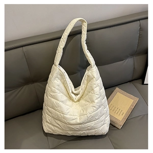 Detail shot of white quilted tote bag featuring a puffer texture on a grey leather sofa
