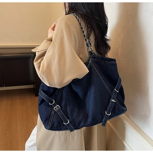 Detail of vintage denim shoulder bag with white stitching and metal chain strap worn by model