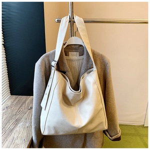 Detail of creamy white leather tote bag hanging on a rack with a brown suit jacket