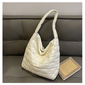 Close-up of a white quilted tote bag with soft padding on a grey leather sofa