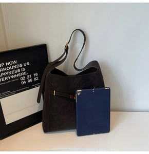 Detail of dark brown suede bucket bag with adjustable strap and tablet for size reference