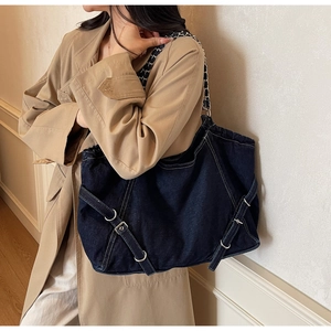 Detail view of large dark blue denim tote bag with silver chain strap and belt buckle