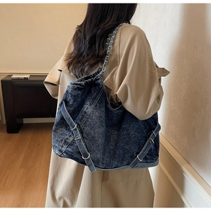 Detailed close-up of dark blue washed denim tote bag with silver chain and buckle accents