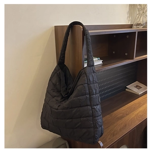 Close-up of black quilted tote bag with bubble texture hanging by a wooden bookshelf