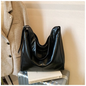 Detail of glossy black hobo tote bag with visible stitching and adjustable strap on a suitcase