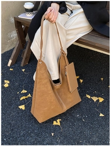 Detail of brown suede tote bag with white stitching shown in an autumn outdoor setting