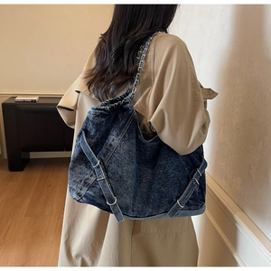 Detail of blue washed denim shoulder bag with chain strap worn with a trench coat