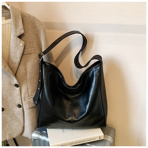 Detail of a black leather hobo bag with adjustable silver buckle strap on a silver suitcase