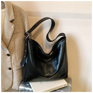 Close-up of black glossy leather hobo bag with wide adjustable shoulder strap and silver buckle