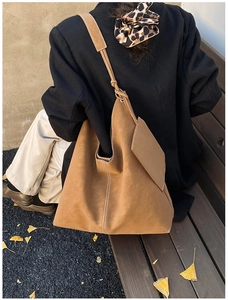 Detail of a vintage tan tote bag with white stitching and envelope pouch on a park bench