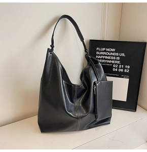 Close-up of black leather tote bag featuring contrast white stitching and a detachable pouch