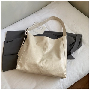 Detail of minimalist cream hobo bag showing soft pleated leather texture on a grey blazer