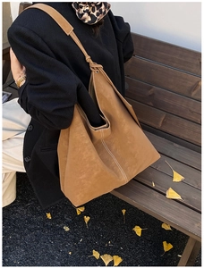 Brown suede tote bag with knotted strap detail shown on a wooden bench with autumn leaves