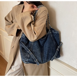 Detail of blue washed denim tote bag with metal chain strap and belt buckle accent