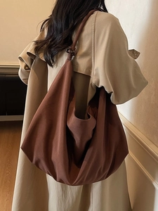 Large brown canvas hobo bag with unique bead detail worn over a stylish trench coat