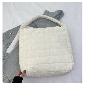 Macro view of white quilted puffer texture and wide shoulder strap on the tote bag