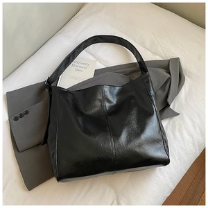 Close-up of black glossy leather tote bag with stitch detail on grey blazer