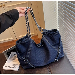 Detail of a large dark blue denim tote bag with metal chain handles and drawstring closure